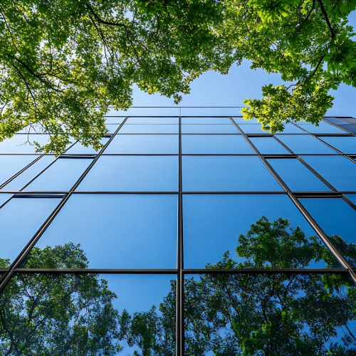 Modern glass building reflecting green trees and blue sky